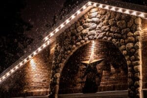 White Christmas lights line a snowy stone and brick gable with a large star mounted below.