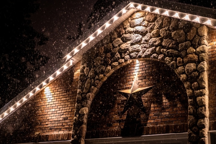 White Christmas lights line a snowy stone and brick gable with a large star mounted below.