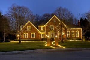 Brick home illuminated with warm white Christmas lights, outlining the roof, windows, and walkway. Professional Christmas light installation creates a festive glow.