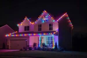 Multicolored Christmas lights outline a house at night, with a wreath above the porch.