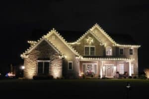 Christmas lights outline a two-story house, with wreaths on the windows and doors.