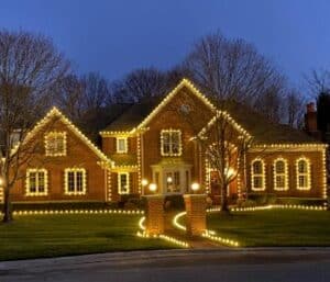 Warm white Christmas lights outline a brick house, its windows and the curved walkway to the entrance.
