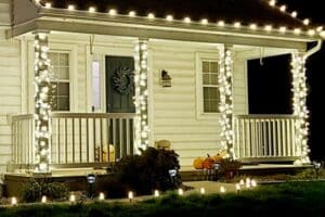 White Christmas lights wrap porch columns and line the roof edge and path, with pumpkins beside the front steps.