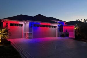 Red, white and blue lights illuminate the roof edge above garage doors at dusk.