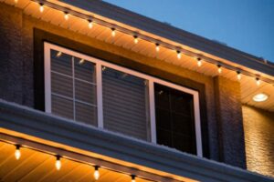Warm white bulbs hang beneath two roof edges around a second-story window.