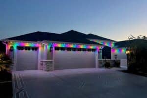 A modern home is illuminated with colorful Christmas lights outlining the roofline, showcasing a potential Christmas light installation cost for homeowners.