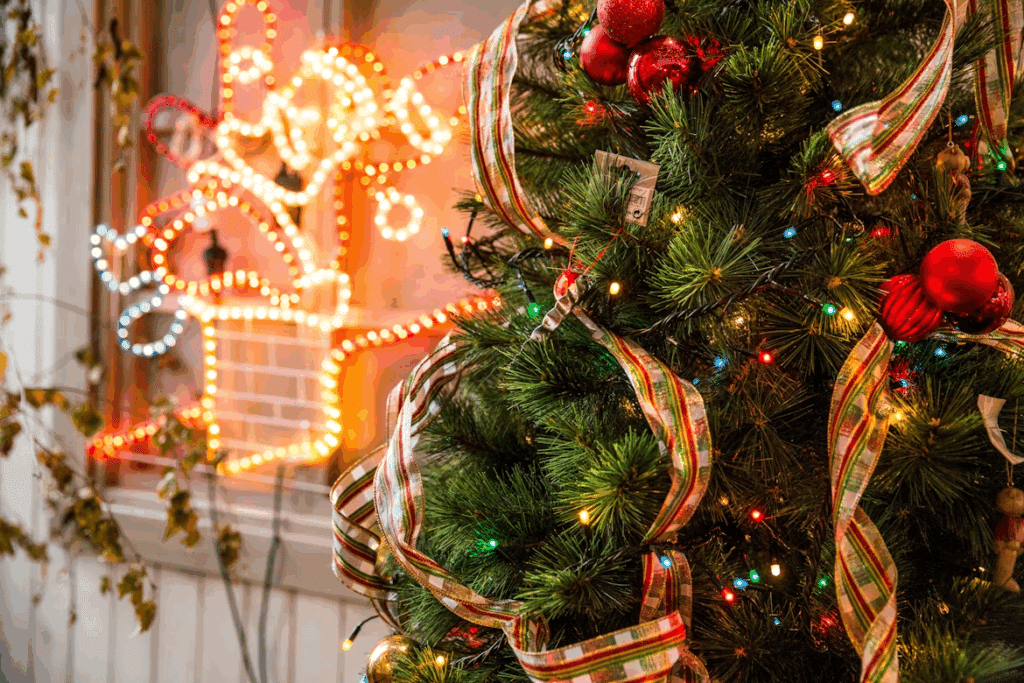 Close-up of a decorated Christmas tree with red and gold ornaments, colorful lights, and a plaid ribbon, with a star-shaped light fixture visible in the background, showcasing winter home exterior upgrades for year-round appeal.