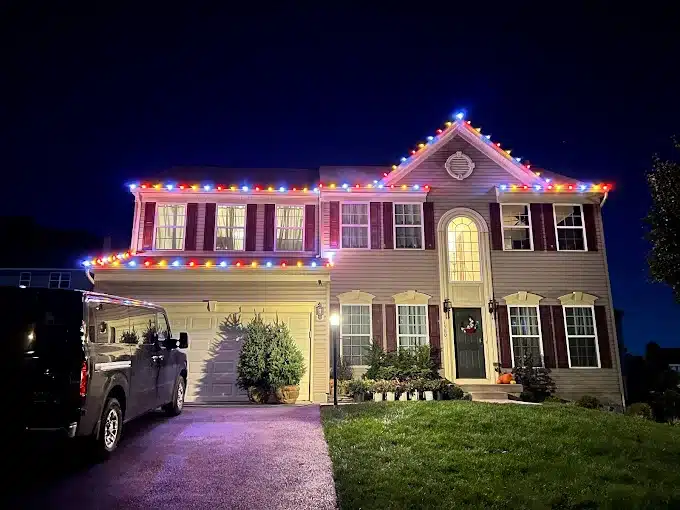 Multicolored Christmas lights trace the roofline of a two-story house at night.