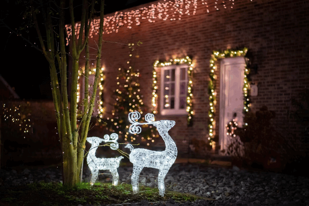 Two illuminated wireframe reindeer stand in front of a brick house adorned with Christmas lights. The festive scene captures the magical holiday display with lights framing the door, window, and roofline.
