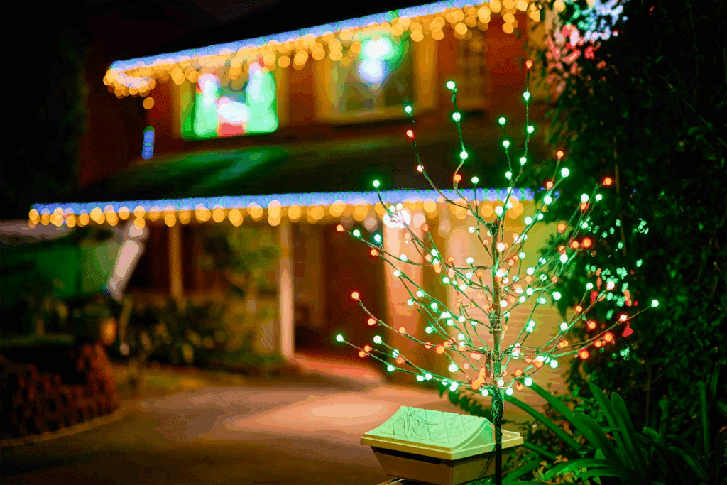 Festive Christmas lights adorn a house at night, showcasing a dazzling holiday display. A small decorative tree with red and green lights sits in the foreground, adding to the cheerful ambiance of the roof's Christmas lights.