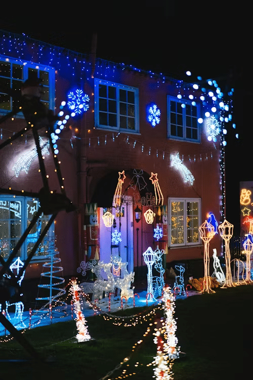 House decked out with bright Christmas lights, including snowflakes, shooting stars, and reindeer, illuminating the yard for the holiday season.