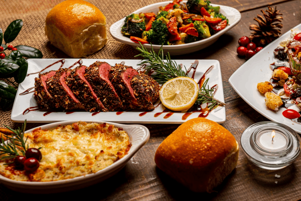 A Christmas dinner spread includes sliced roast beef, vegetables, casserole and dinner rolls on a wooden table.