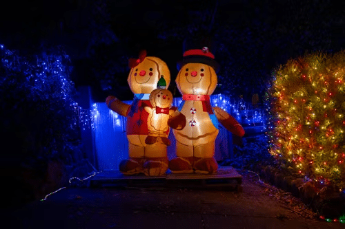 Inflatable gingerbread family Christmas decoration: mother, father, and child, lit up against a dark background of blue and red holiday lights.
