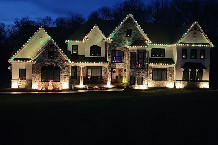 Large house at night decorated with Christmas lights outlining the roof, windows, and landscaping. Snowmen decorations are on the front lawn.