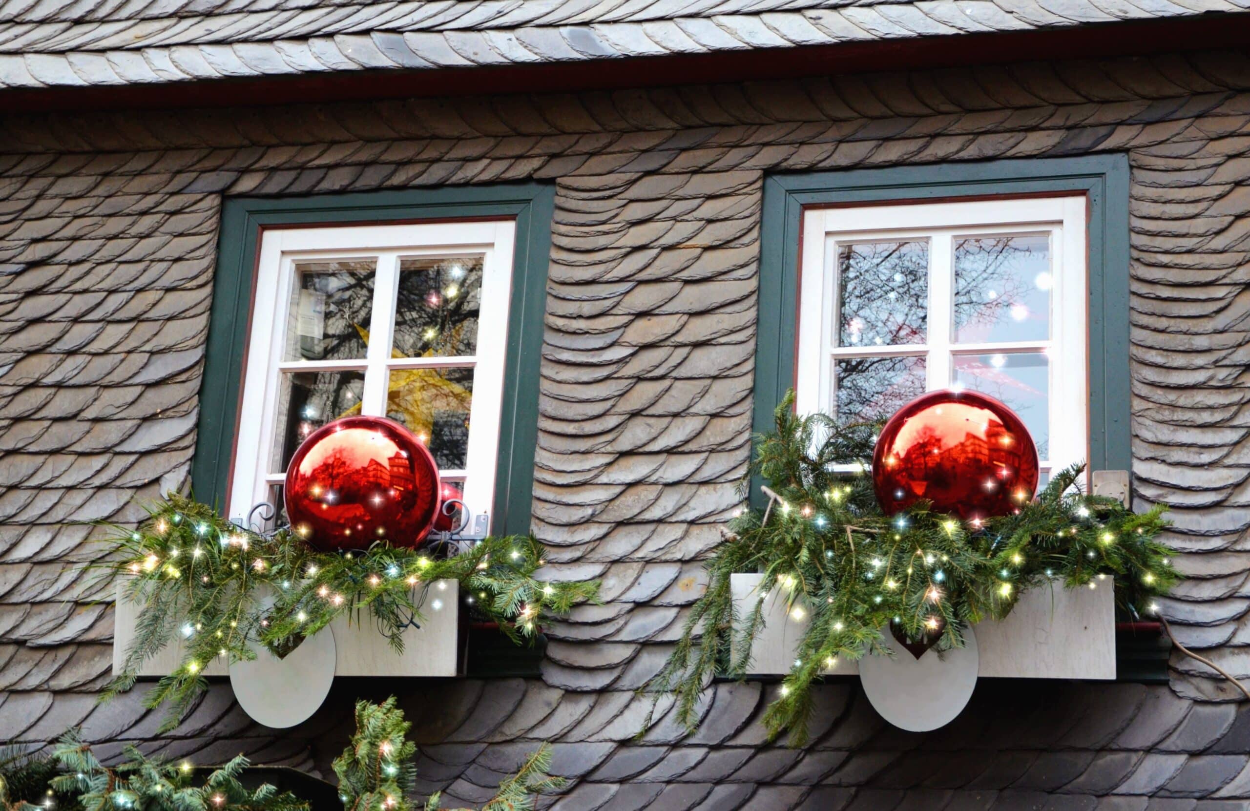 Two windows decorated for Christmas with red ornaments, evergreen boughs, and twinkling lights. A charming, festive scene for DIY Christmas decorations.