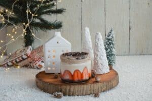 Festive Christmas dessert jar with strawberries and chocolate, set on a wooden slice with snowy decor, a mini Christmas tree, a ceramic house, and wrapped gifts. A cozy DIY Christmas decorations scene.