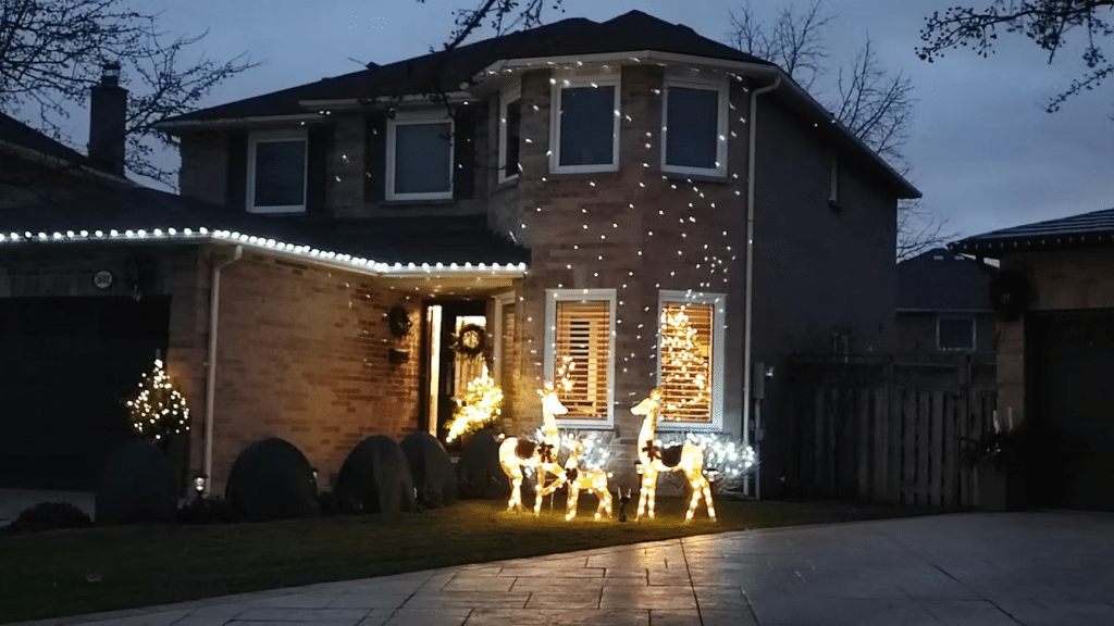 Home adorned with Christmas lights display: roofline lights, window twinkle lights, and illuminated reindeer figurines on the lawn create a festive holiday scene.