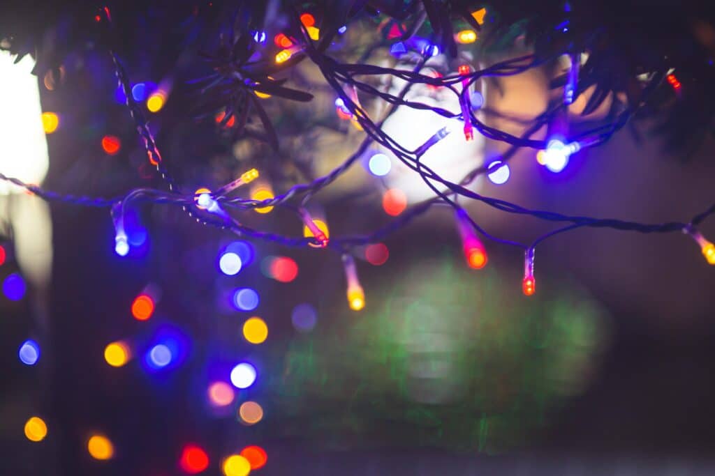 Colorful Christmas lights twinkle on a tree, some in focus, others blurred into bokeh circles of red, blue, and gold. A festive, warm glow helps illustrate how to store Christmas lights without the tangle.