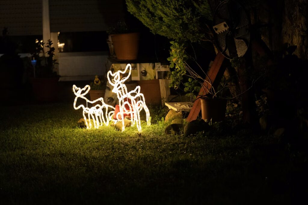 Glowing Christmas lights displays of three illuminated reindeer stand on a dark green lawn at night, bringing holiday cheer to the home.