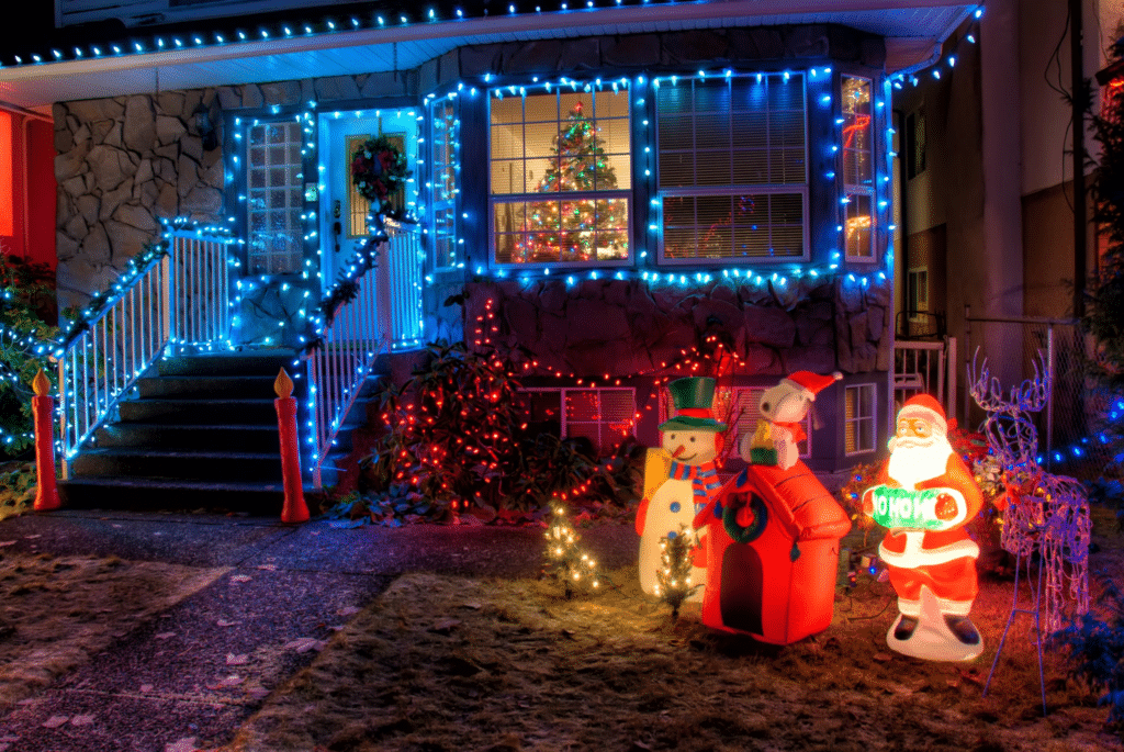 Blue lights line a house’s roof and window, with illuminated Santa, Snoopy and snowman figures on the lawn.