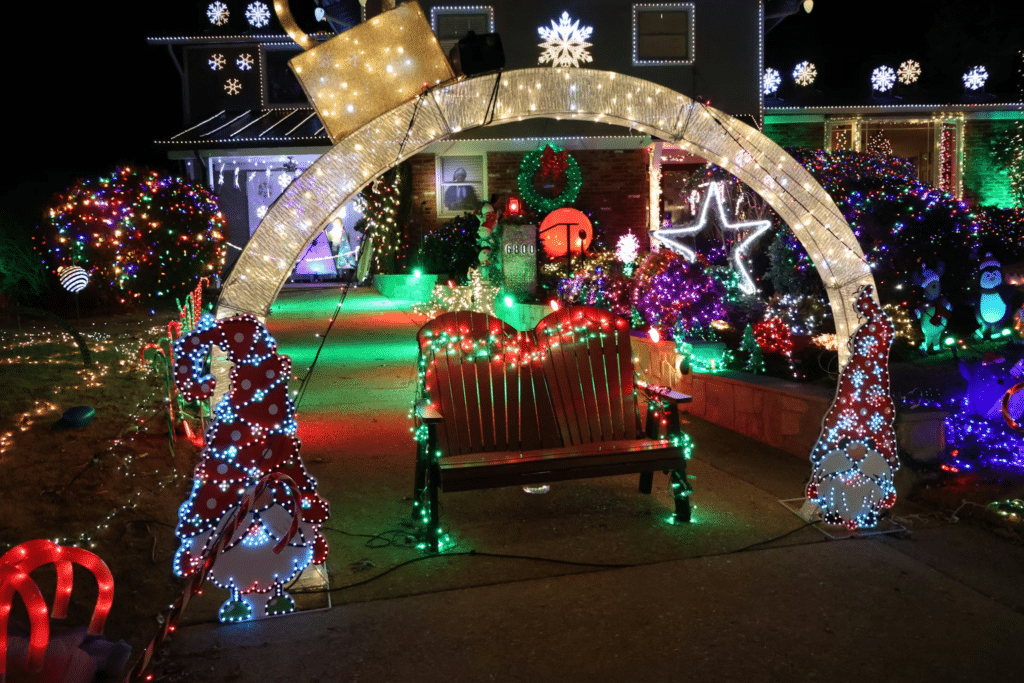 A house display with an illuminated arch, snowmen, and a bench among colorful lights.